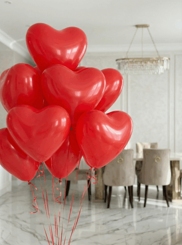 Букет из красных латексных шаров в форме сердца с красными лентами в светлом интерьере.