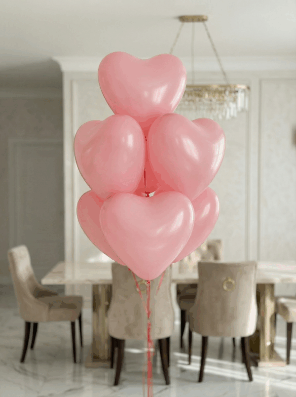 Букет из нежно-розовых латексных шаров в форме сердца с лентами в светлом интерьере.